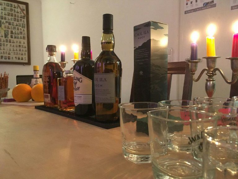 Ein Tisch mit Gläsern, Kerzen, Obst und zentral vier Whiskey-Flaschen
